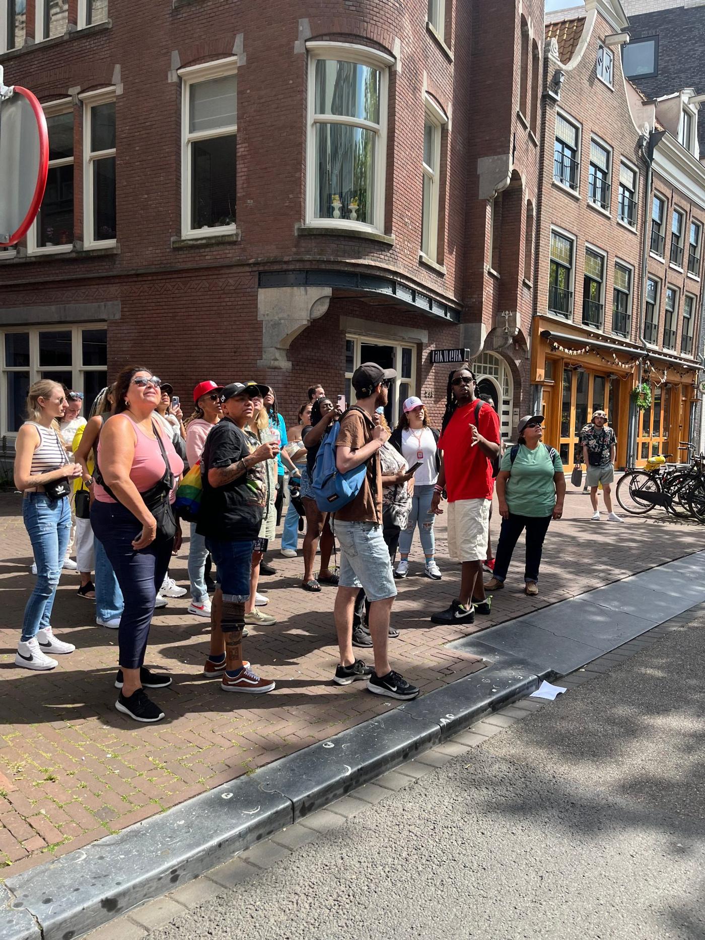 Tour guests looking up at brick facades and a curved gable on an Amsterdam street corner